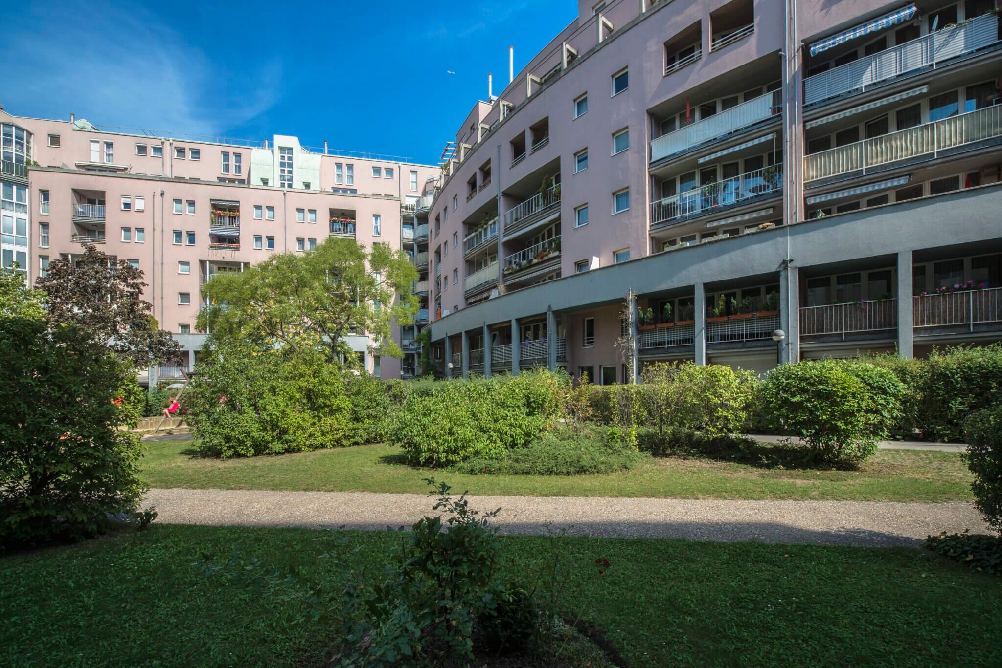 begrünter Innenhof mit asphaltierten Wegen, im Hintergrund das Wohngebäude